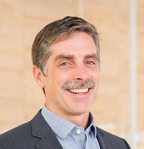 Headshot of Tim Sexton, smiling and wearing a grey suit