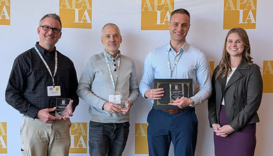Four individuals accepting the award, standing in front of a background with yellow APA logos.