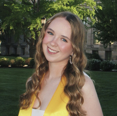 Headshot of Molly McCarthy wearing a white top and a yellow graduation stole